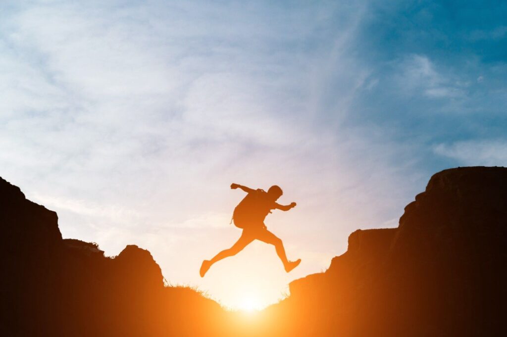 Person jumping between cliffs at sunrise symbolizing personal development and self growth