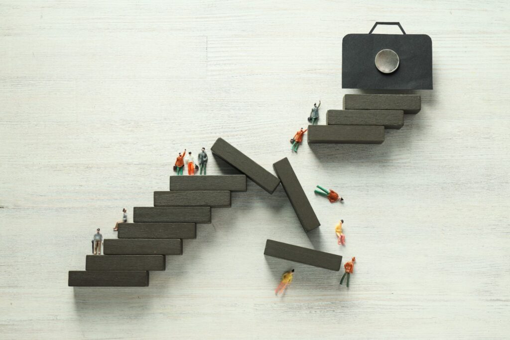 Miniature figures climbing uneven blocks towards a briefcase symbolizing career growth and overcoming obstacles